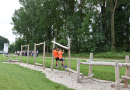 Kinder auf einem Spielplatz mit einem Gerät aus runden Holzbalken zum Klettern und Balancieren.